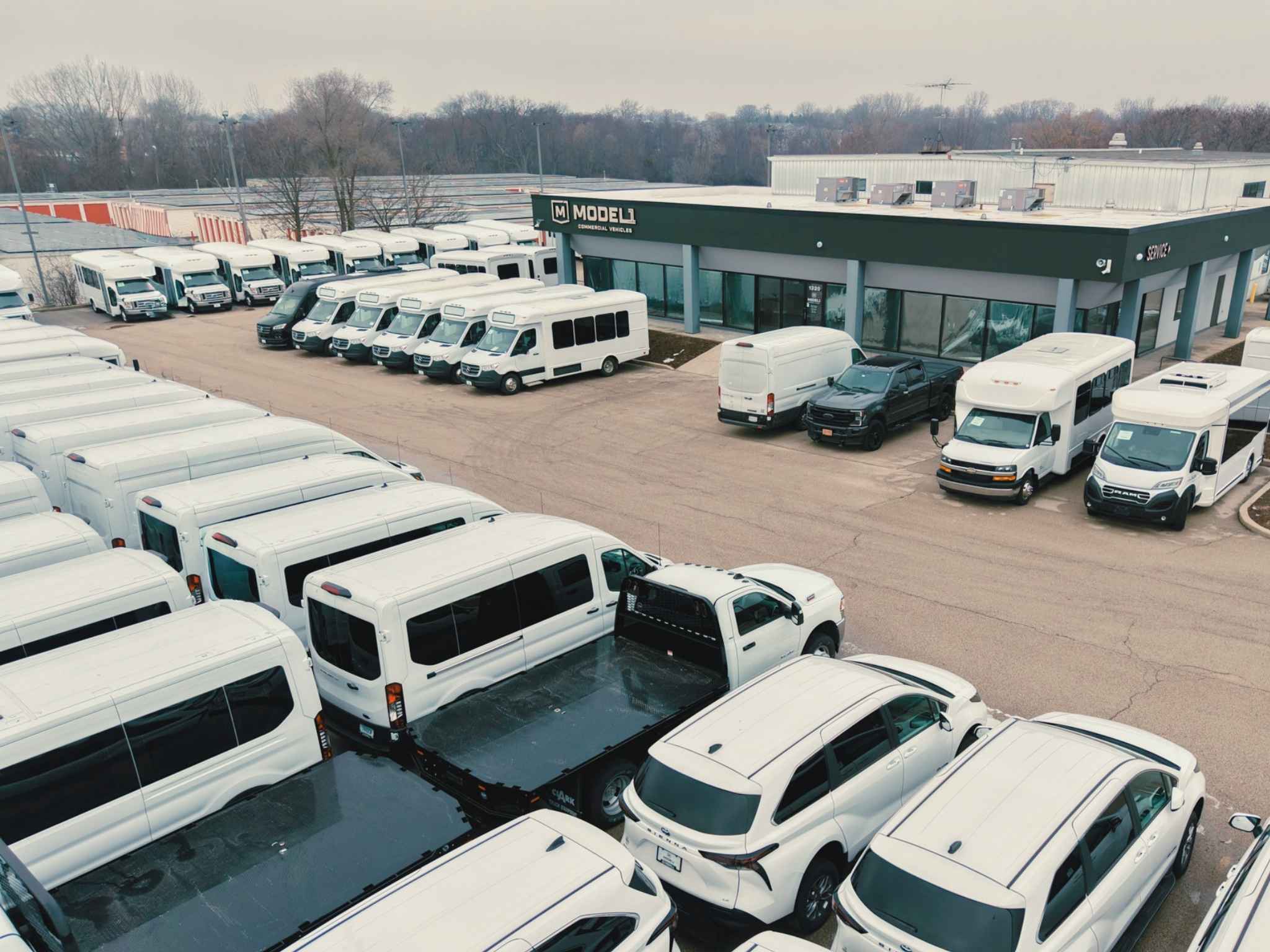 fleet of buses and vans in white parked in front of a Model 1 store in Elgin